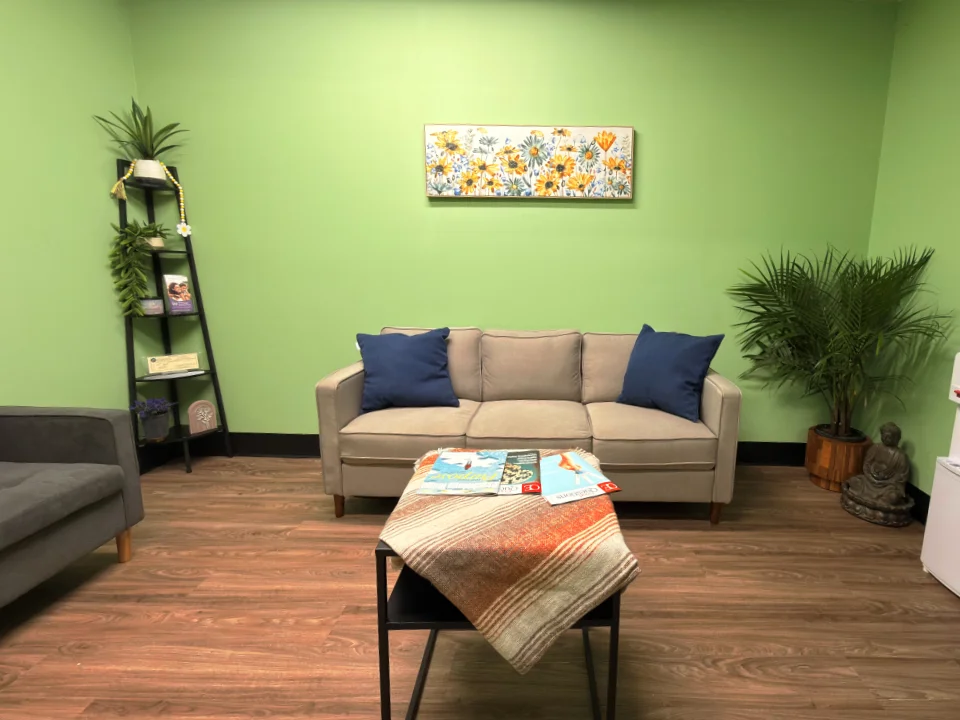 The waiting room at Healing TMS Clinic — beige sofa, plants, and warm wood floors.